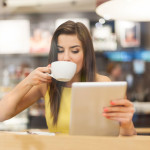 Woman having a cup of coffee, while reading a tablet.
